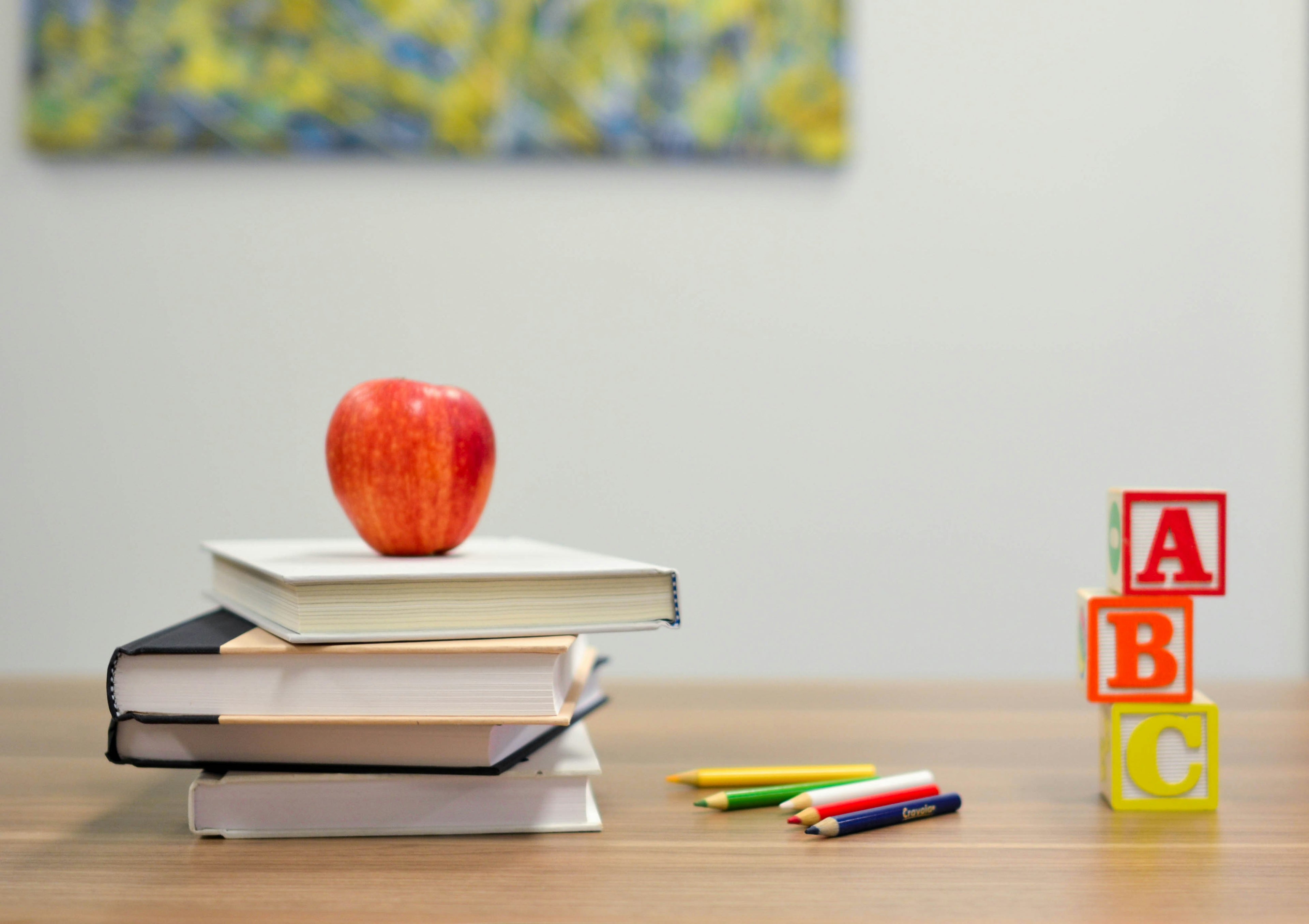 Stack of books with an apple, colored pencils, and ABC blocks on a desk